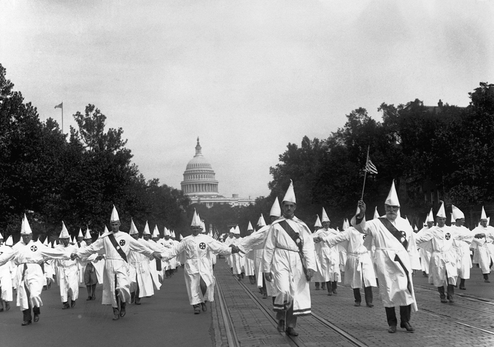 A black-and-white photograph of Ku Klux Klan members marching down the street.