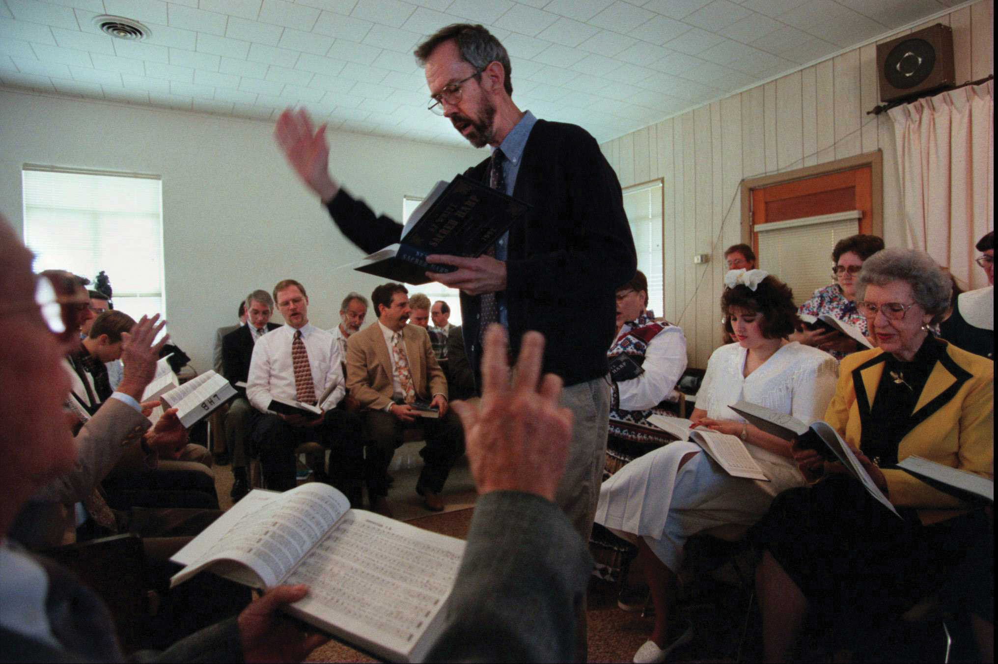 A photo of a man leading singers arranged around him in the traditional square configuration.