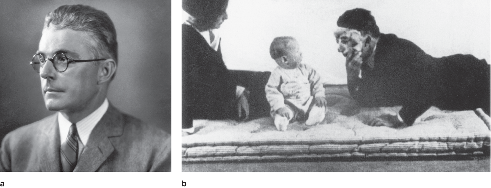 Portrait of John B. Watson. | A photo shows Watson wearing a scary mask and looking at baby Albert who looks shocked. A woman is seated nearby and looks on.