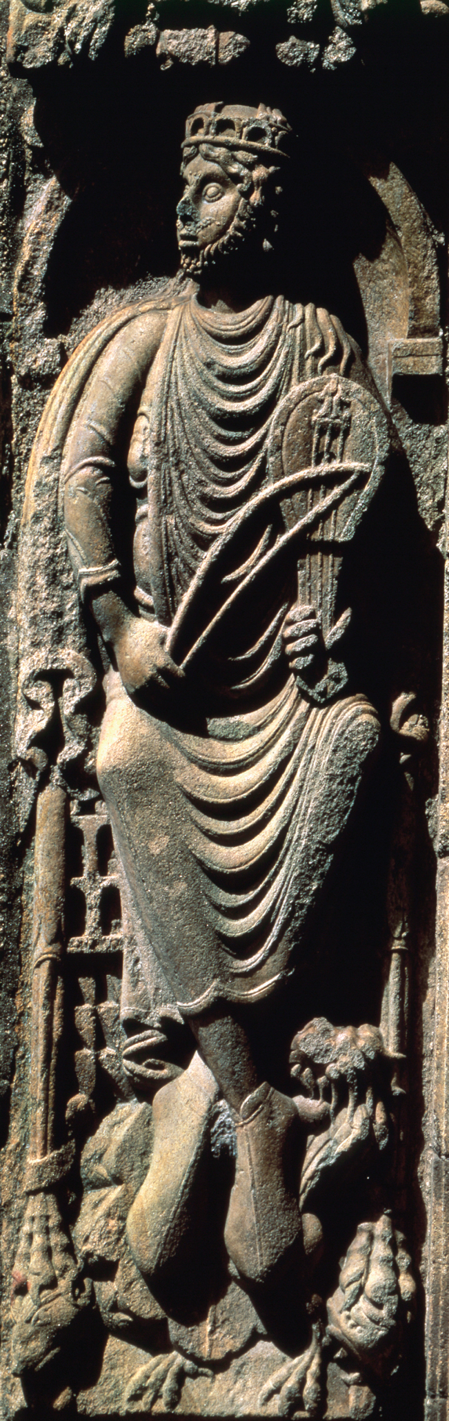 A relief carved into stone depicts King David, with a full beard and a crown, and carrying a stringed instrument and a bow.