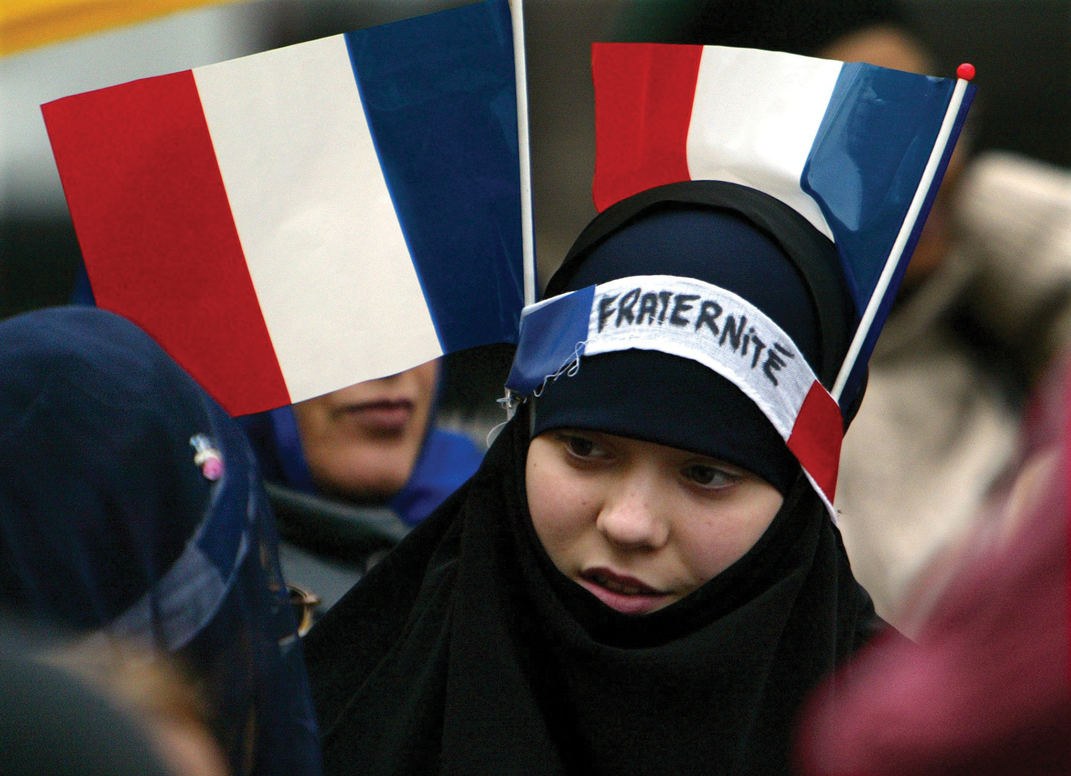 A woman in a crowd wearing a hijab and a headband that reads, “Fraternite.”
