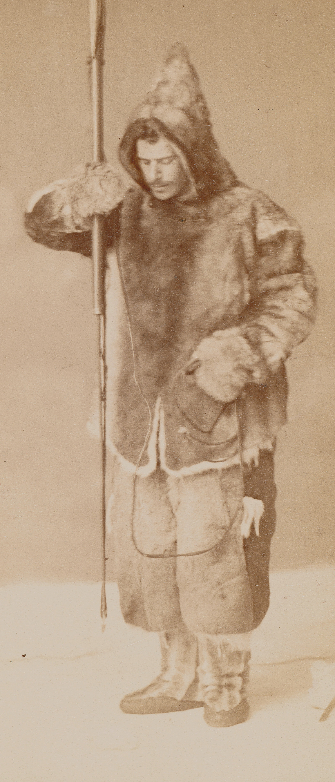 A sepia photograph of Franz Boas, a white man, wearing a hooded fur jacket, fur pants, and high boots holding a spear.
