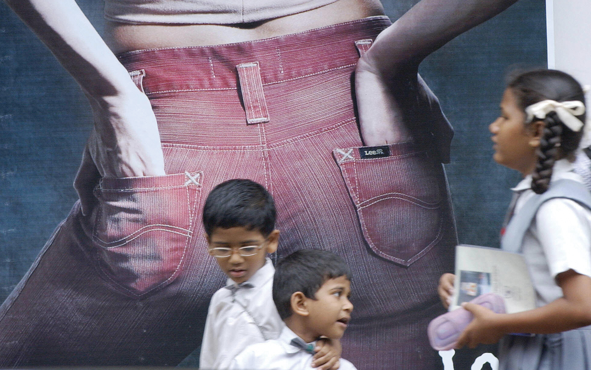 Young children walk past a Lee Jeans advertisement.
