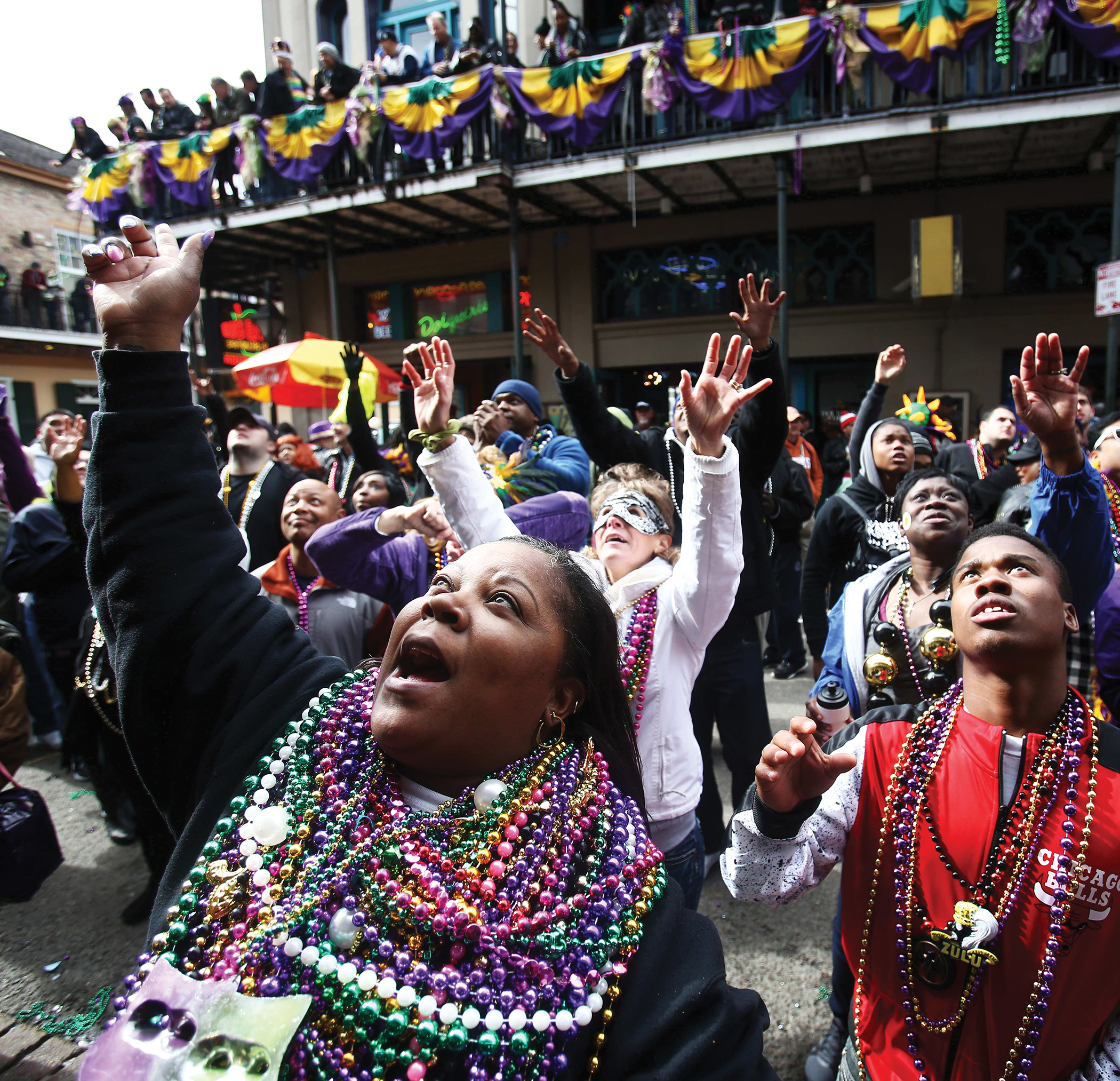A celebration on a street where people are wearing plastic beads around their necks raising their hands toward something.