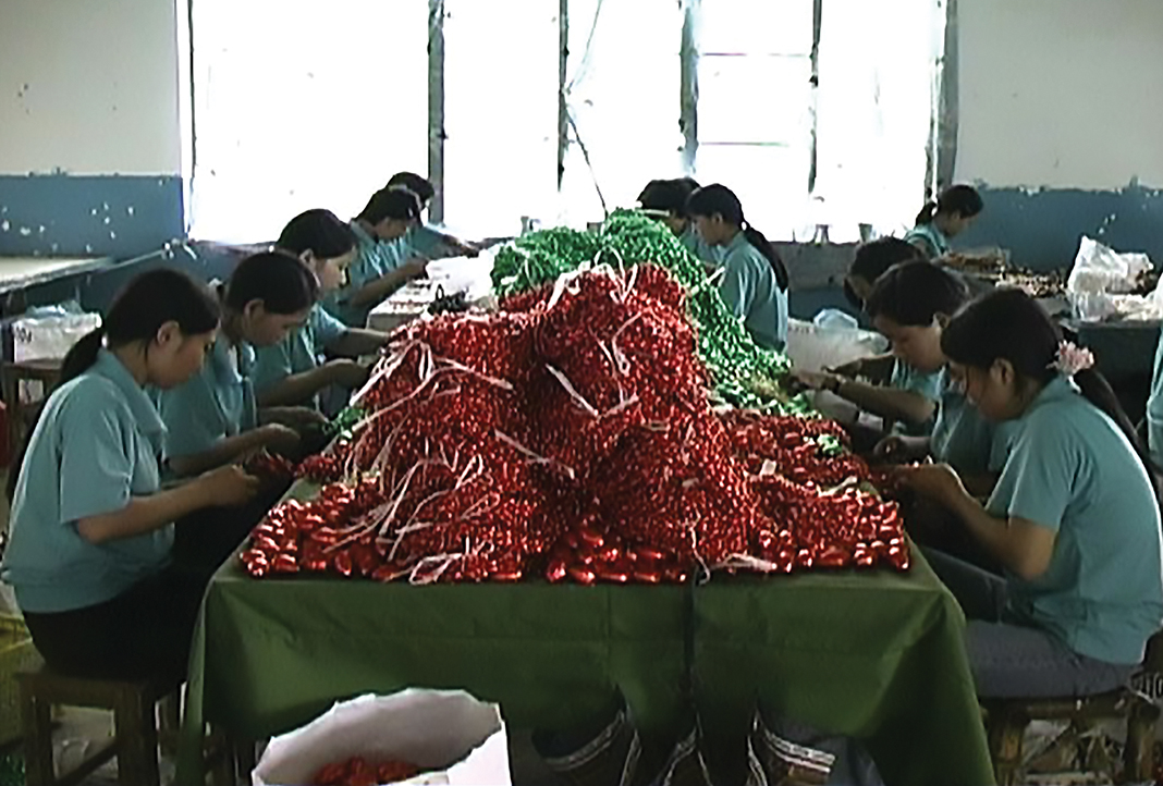 A shabby room where young people sit around a table with giant piles of beads making necklaces.