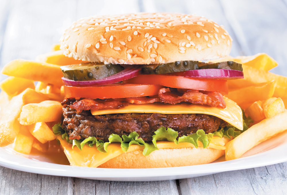 Photo of a bacon cheeseburger with French fries on a plate.