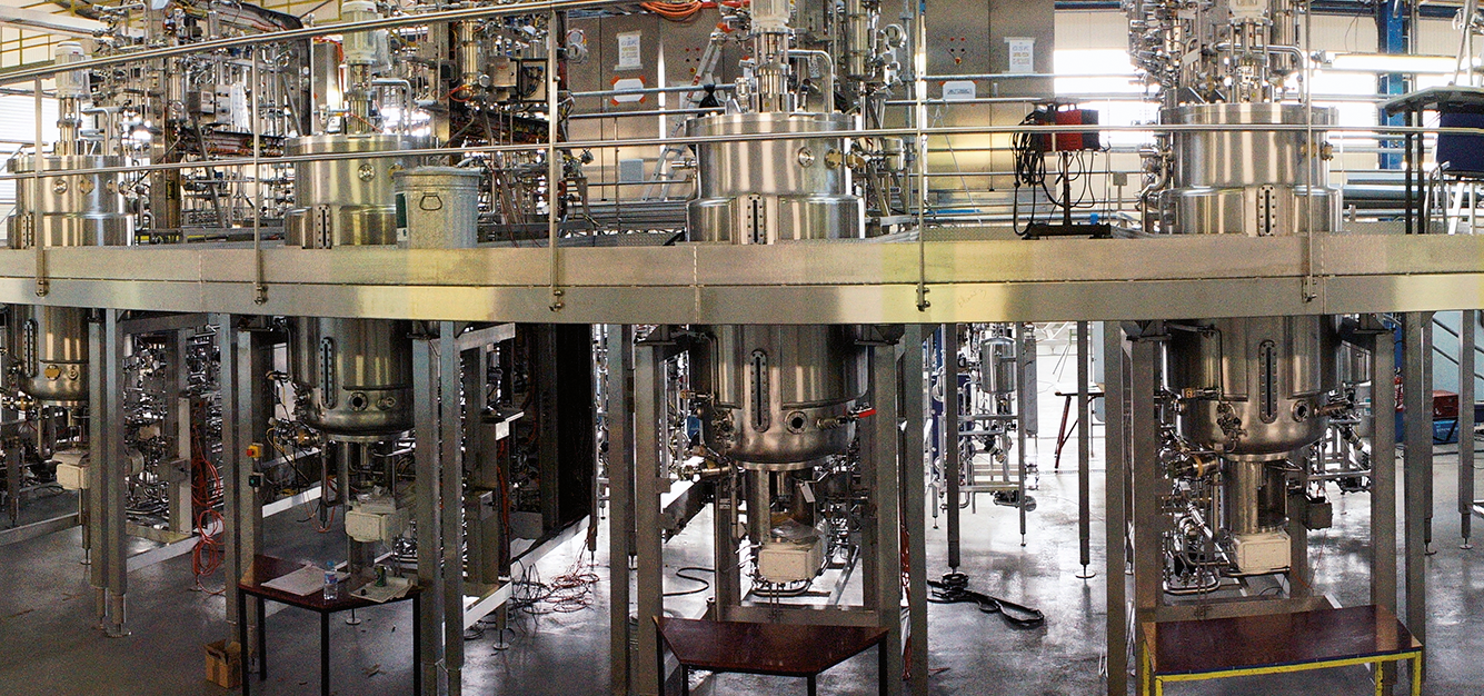 The photograph shows a biotechnology facility with equipment used for processing and producing specific materials.