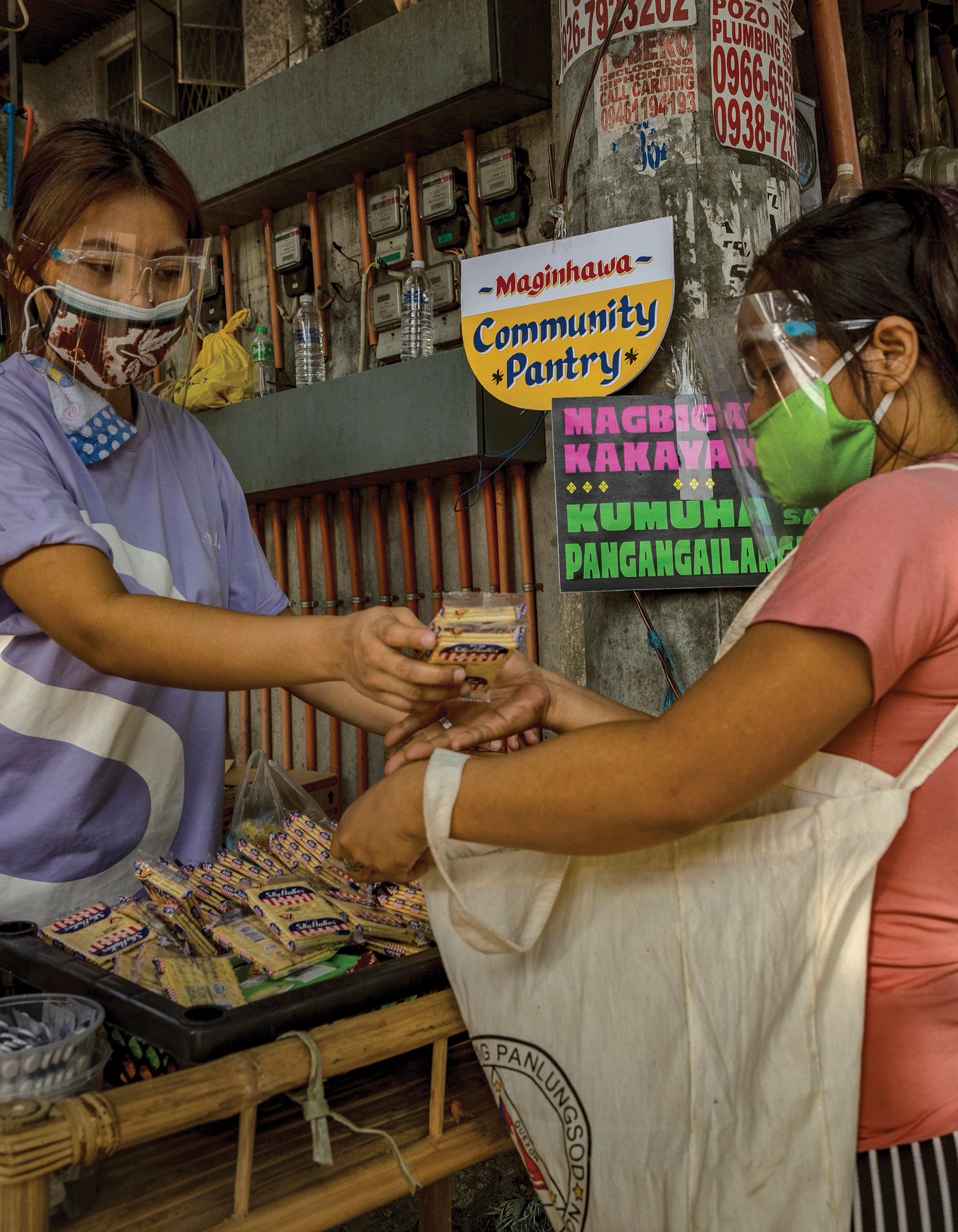 Two women wearing face masks and face shields stand in a food pantry.