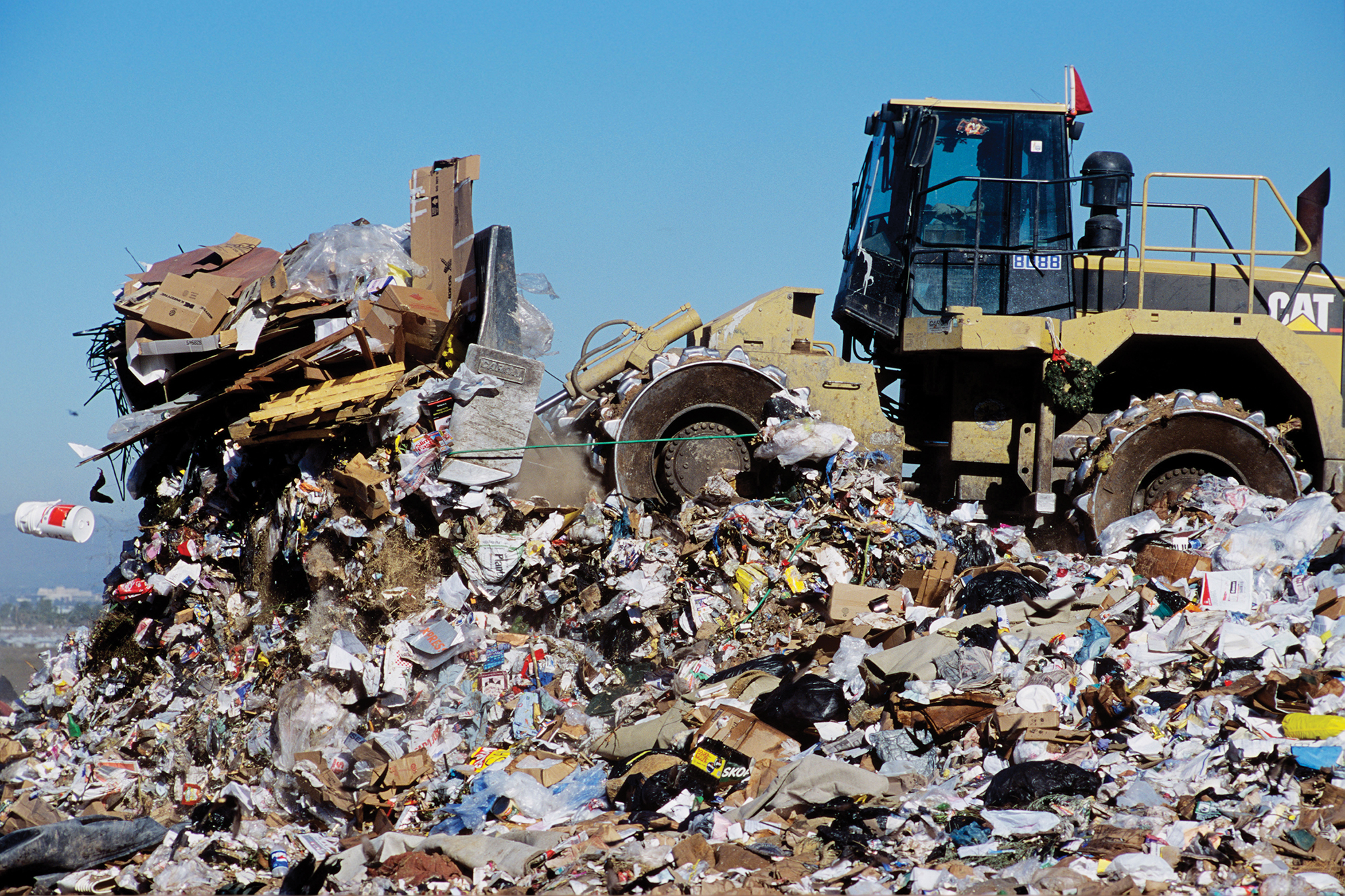 A tractor flattens piles of trash at a dump.