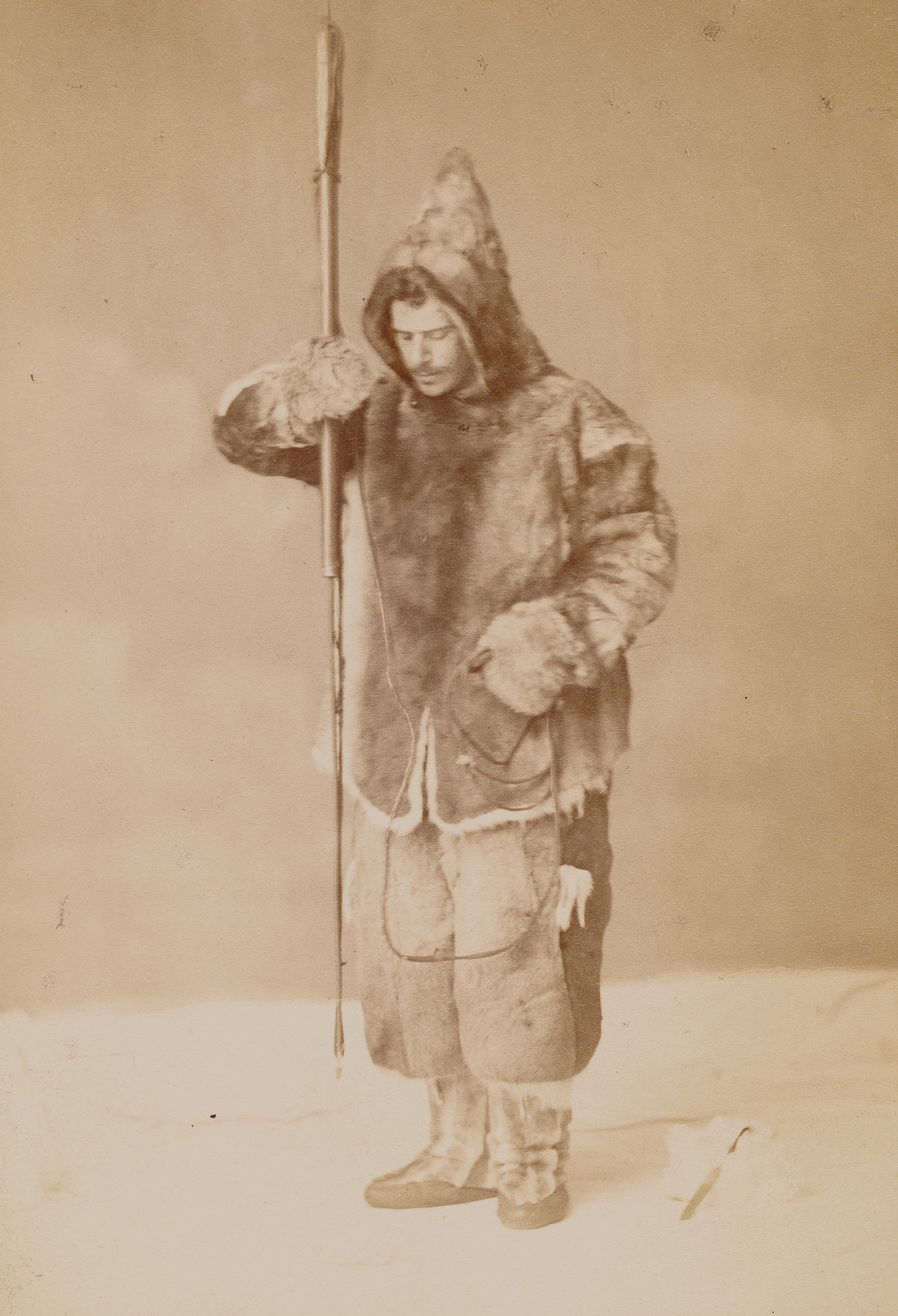 A sepia photograph of Franz Boas, a white man, wearing a hooded fur jacket, fur pants, and high boots holding a spear.