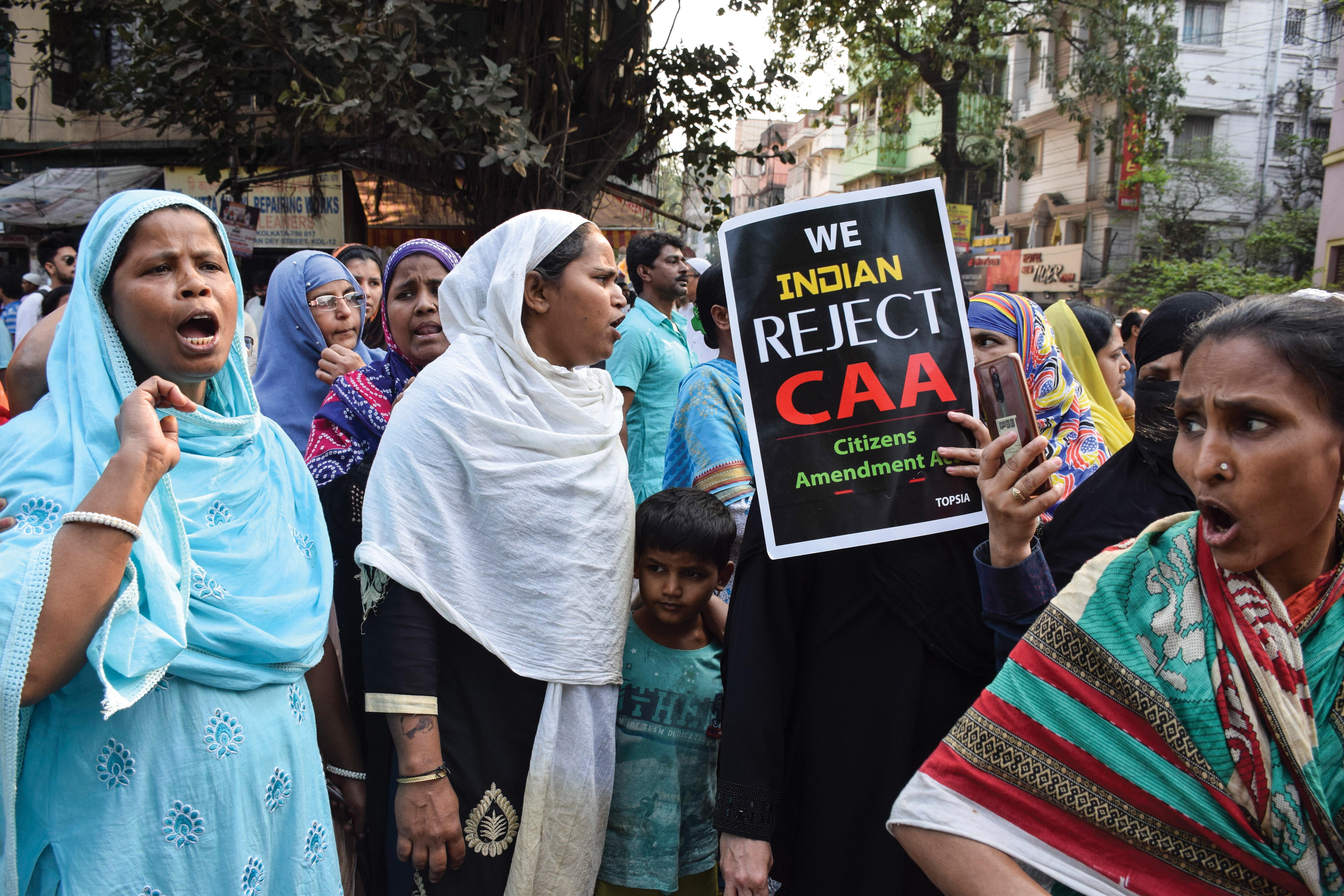 Several women, many wearing hijabs, gather to protest in India. A woman holds a sign that reads: "We Indian Reject CAA (Citizens Amendment Act)."