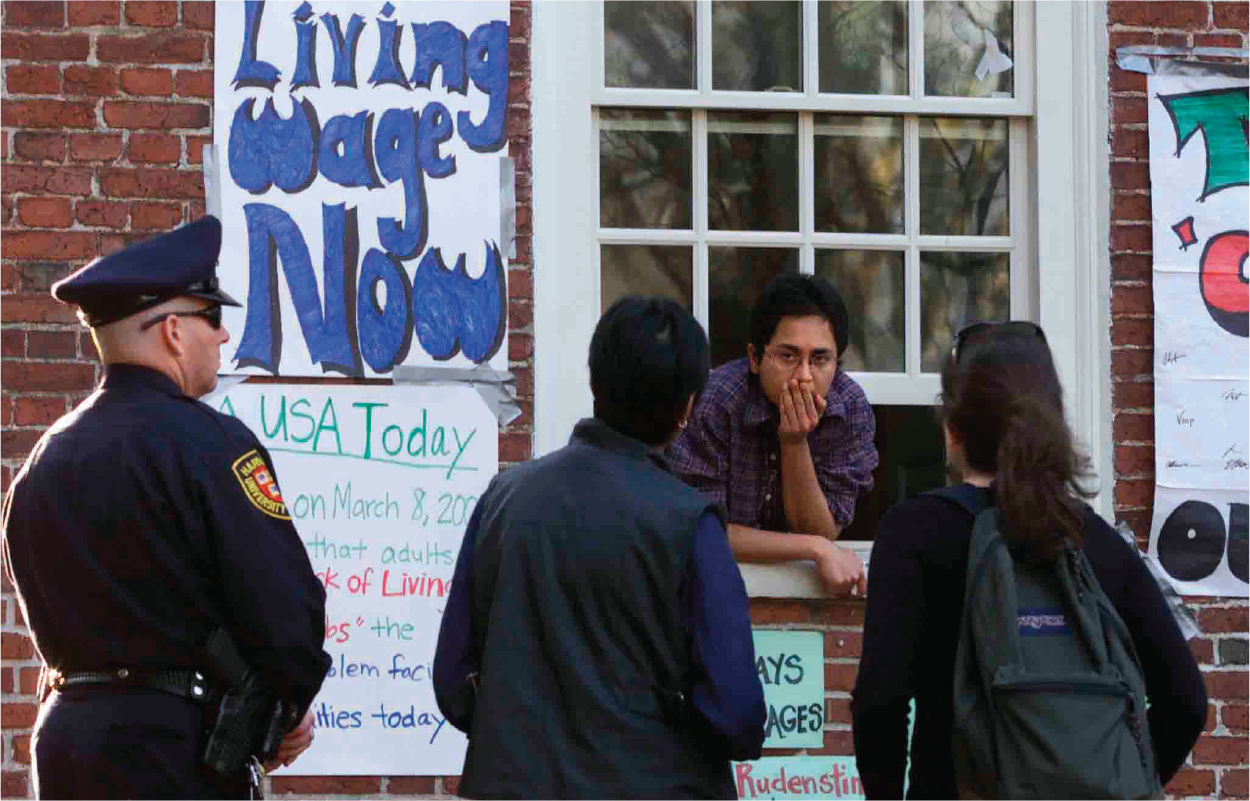 A student leans out through a campus window, around which posters are stuck.
