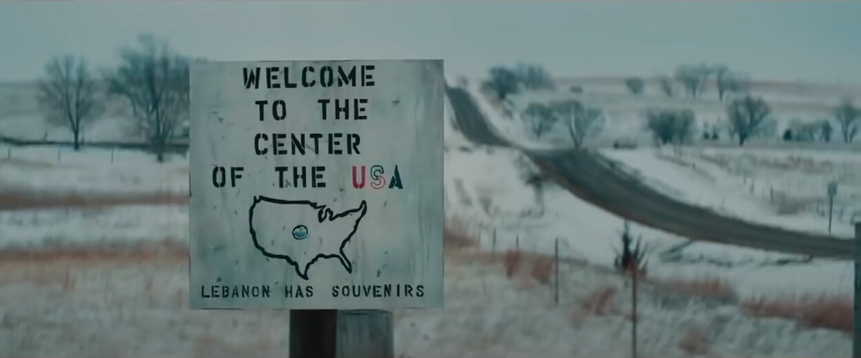 A sign that reads “WELCOME TO THE CENTER OF THE USA” above an outline of the United States with the center marked. Below the outline, the sign reads, “LEBANON HAS SOUVENIRS.”