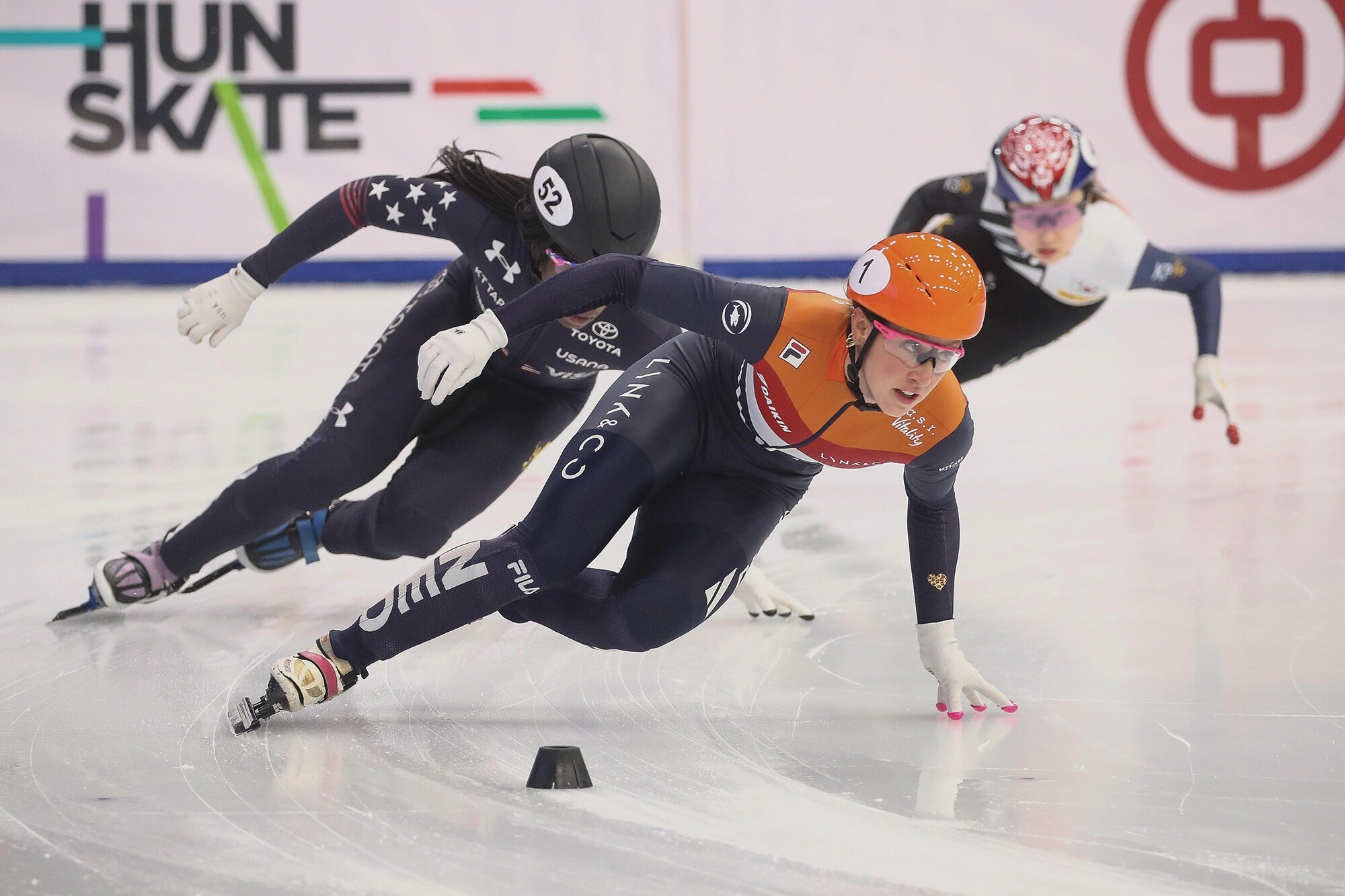 Three short track speed skaters skating making a turn in an ice rink.