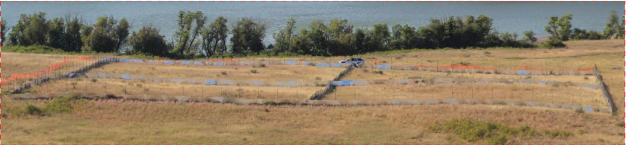 In an open field by a body of water, a large square enclosure has been set up.