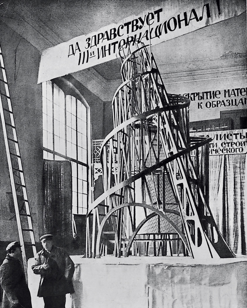 Black-and-white photograph of a large wooden sculpture of a tower within an interior exhibition space.