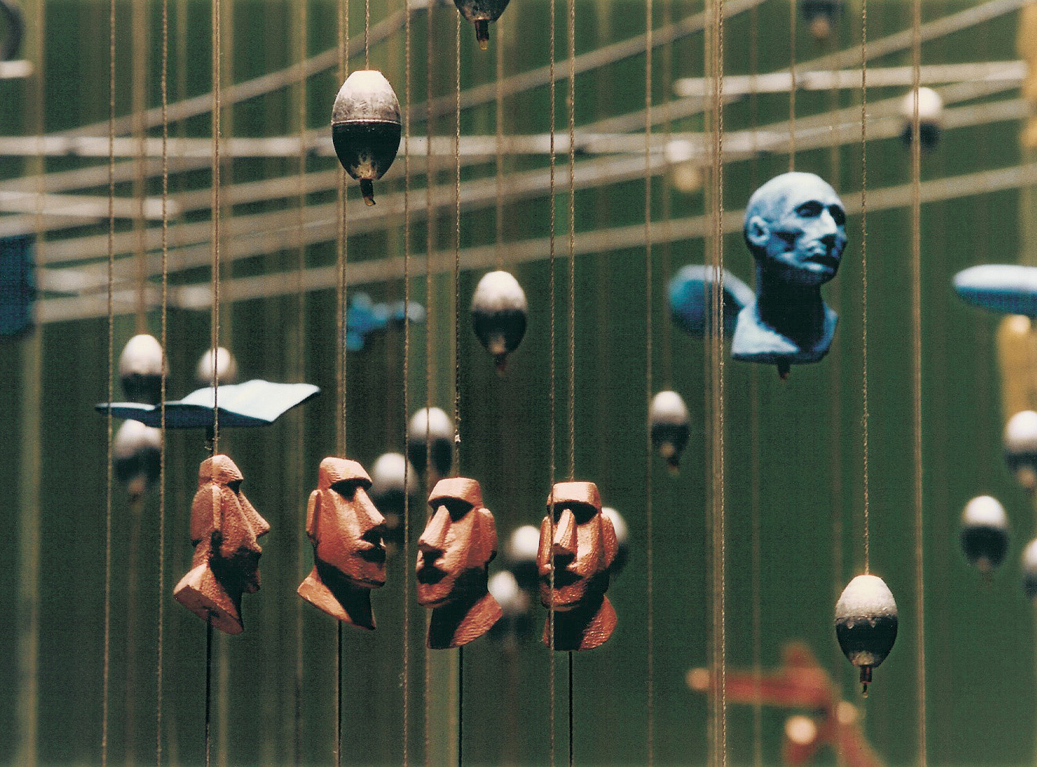 A selection of small red and blue heads, and round objects hang at different lengths on pieces of string.