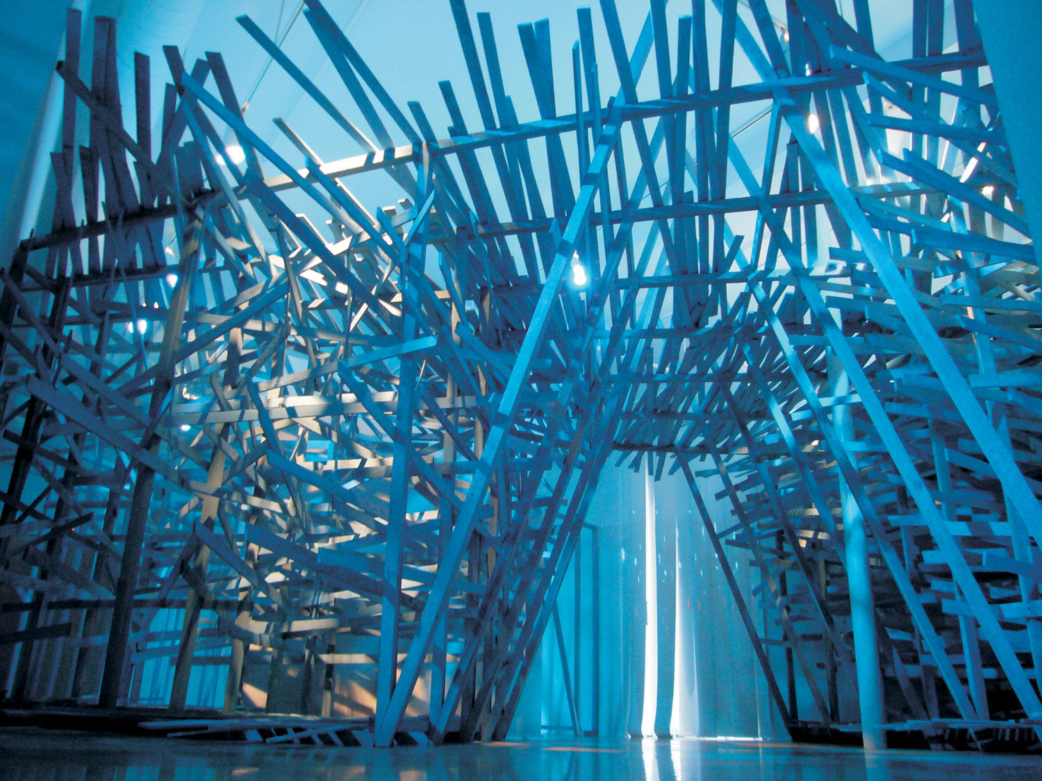 Room-sized installation of wooden slats lit with blue light.