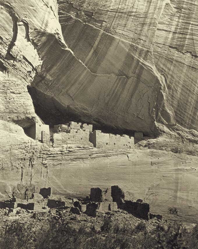 Black and white photo of large rock overhang with small figures beneath.