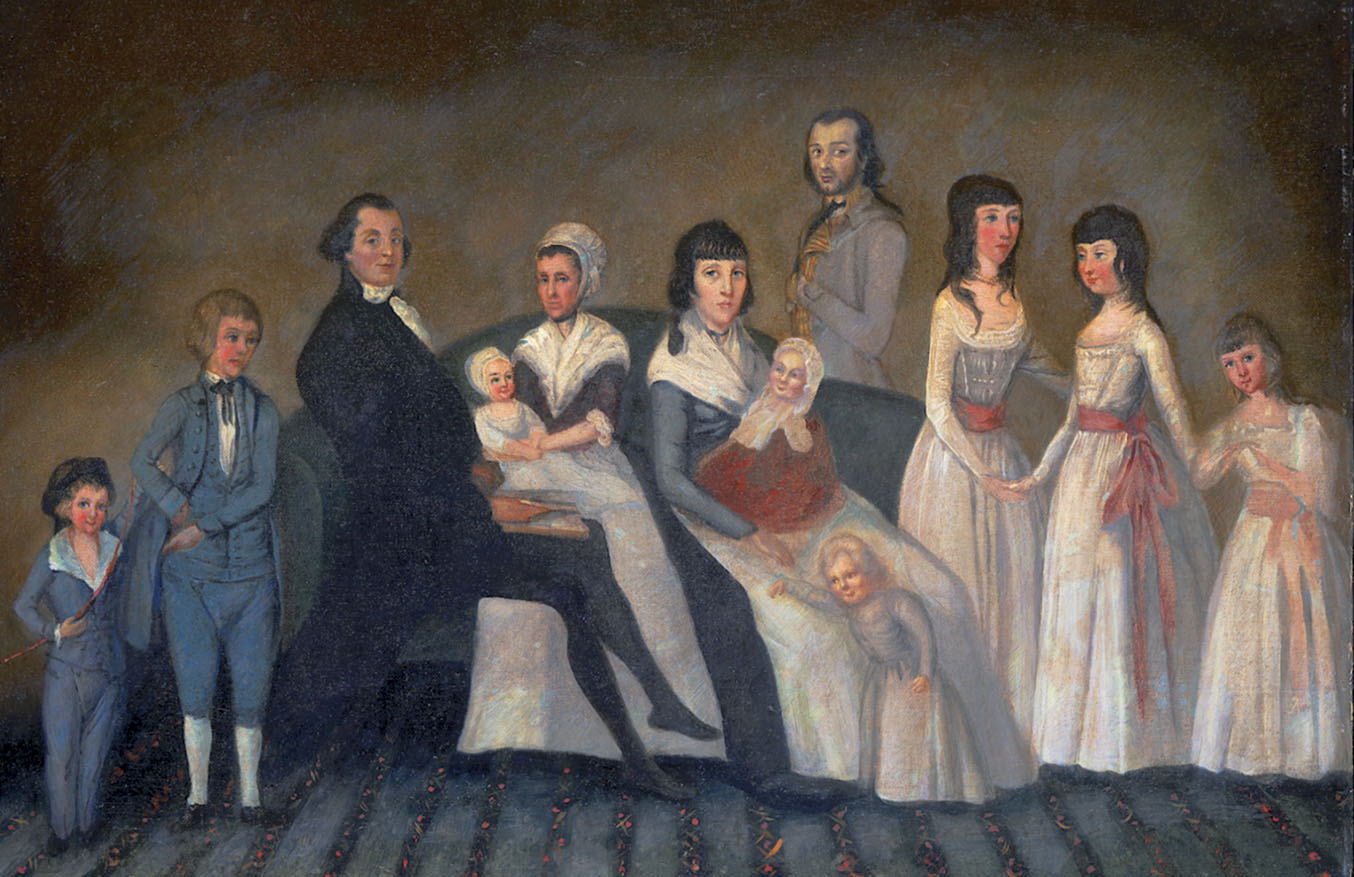 A family portrait. The mother and father sit on a couch, holding a newborn. The other children, ranging from infants to young adults, gather around the couch.
