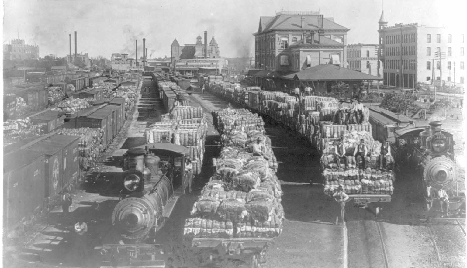 Historical photograph of soldiers and tanks moving through a war-damaged city street lined with destroyed buildings.