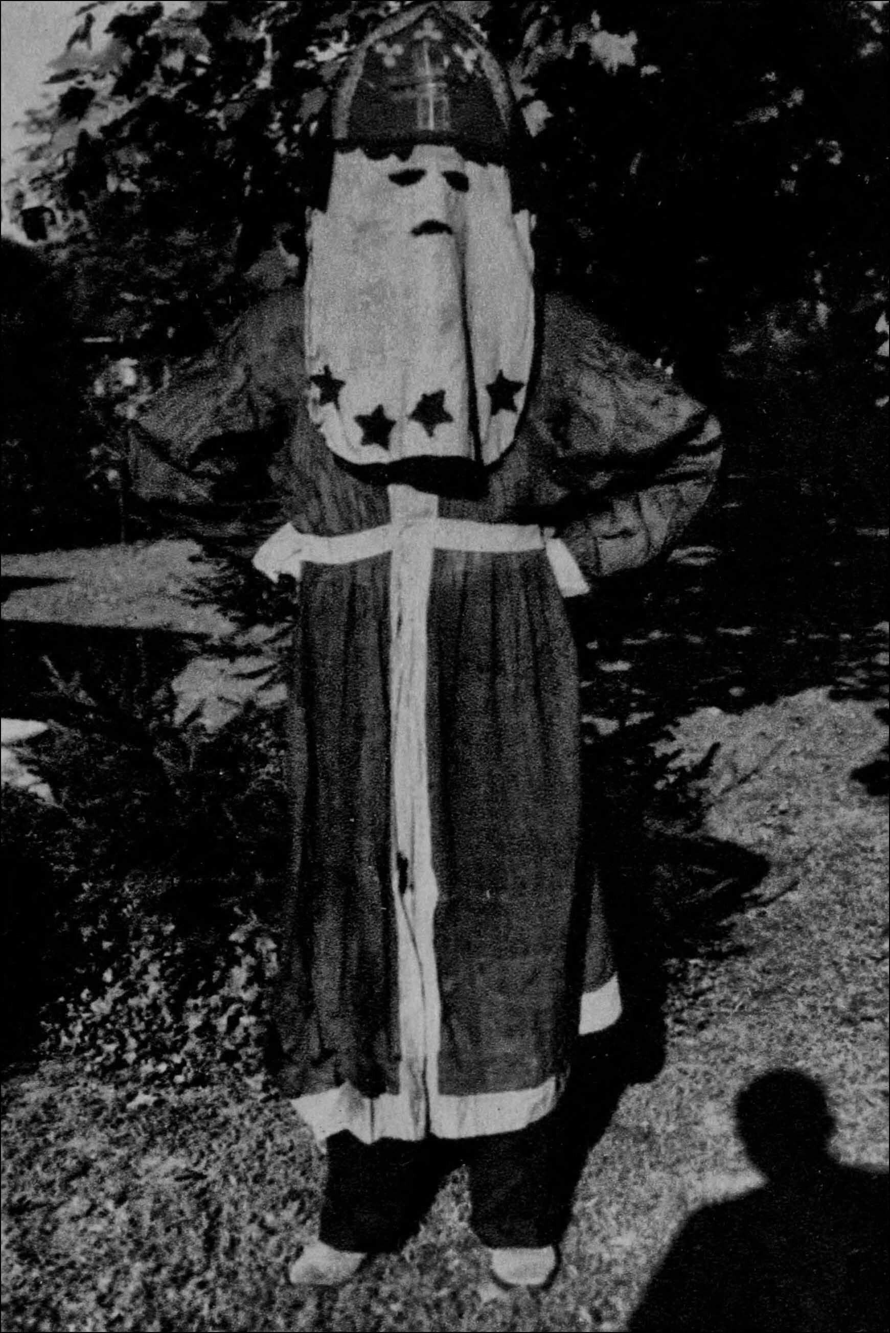 Black-and-white image of a person in ceremonial dress with patterned outfit and head covering.