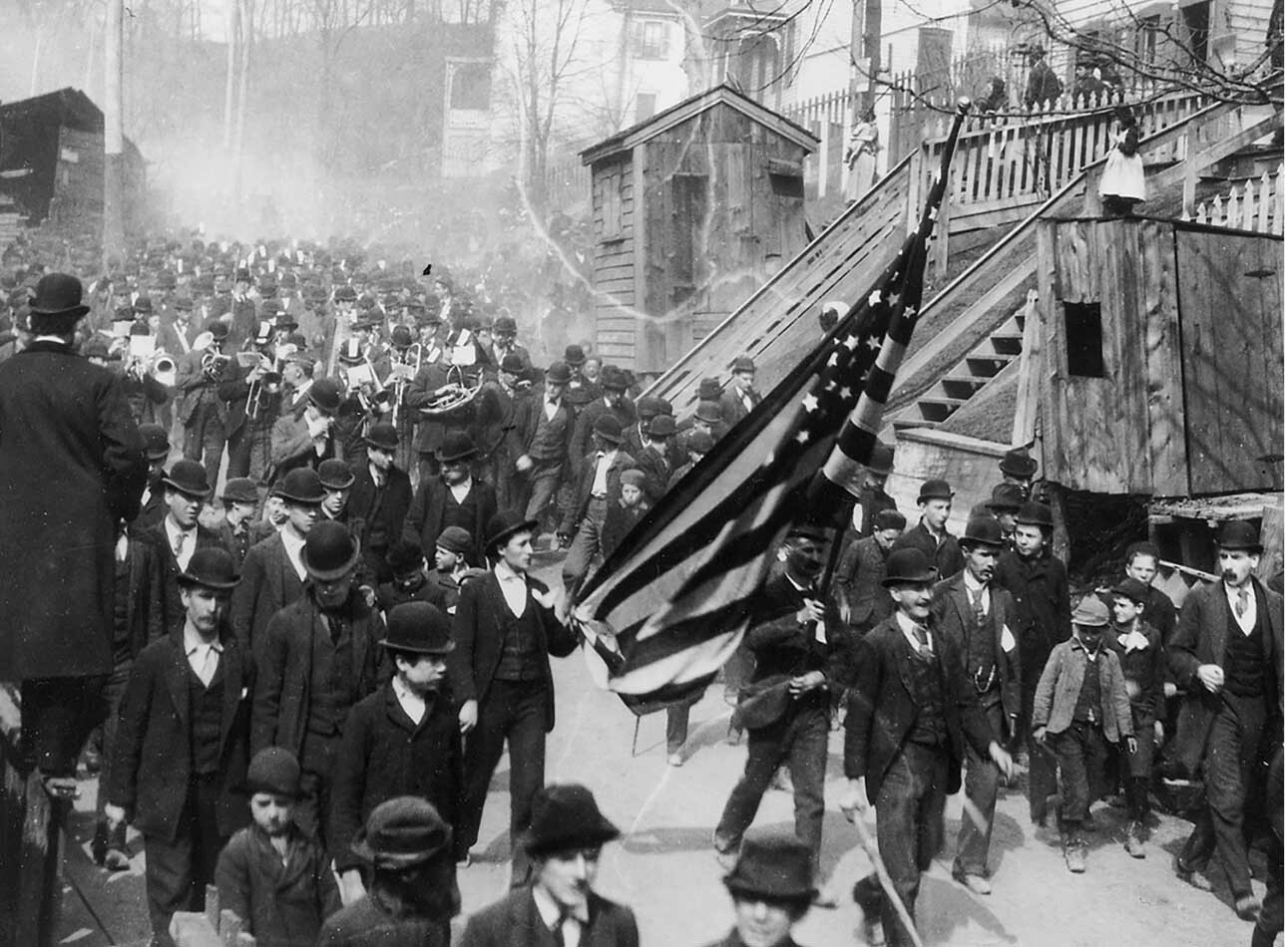 Large crowd gathered in a city street carrying an American flag during a historical parade or demonstration.