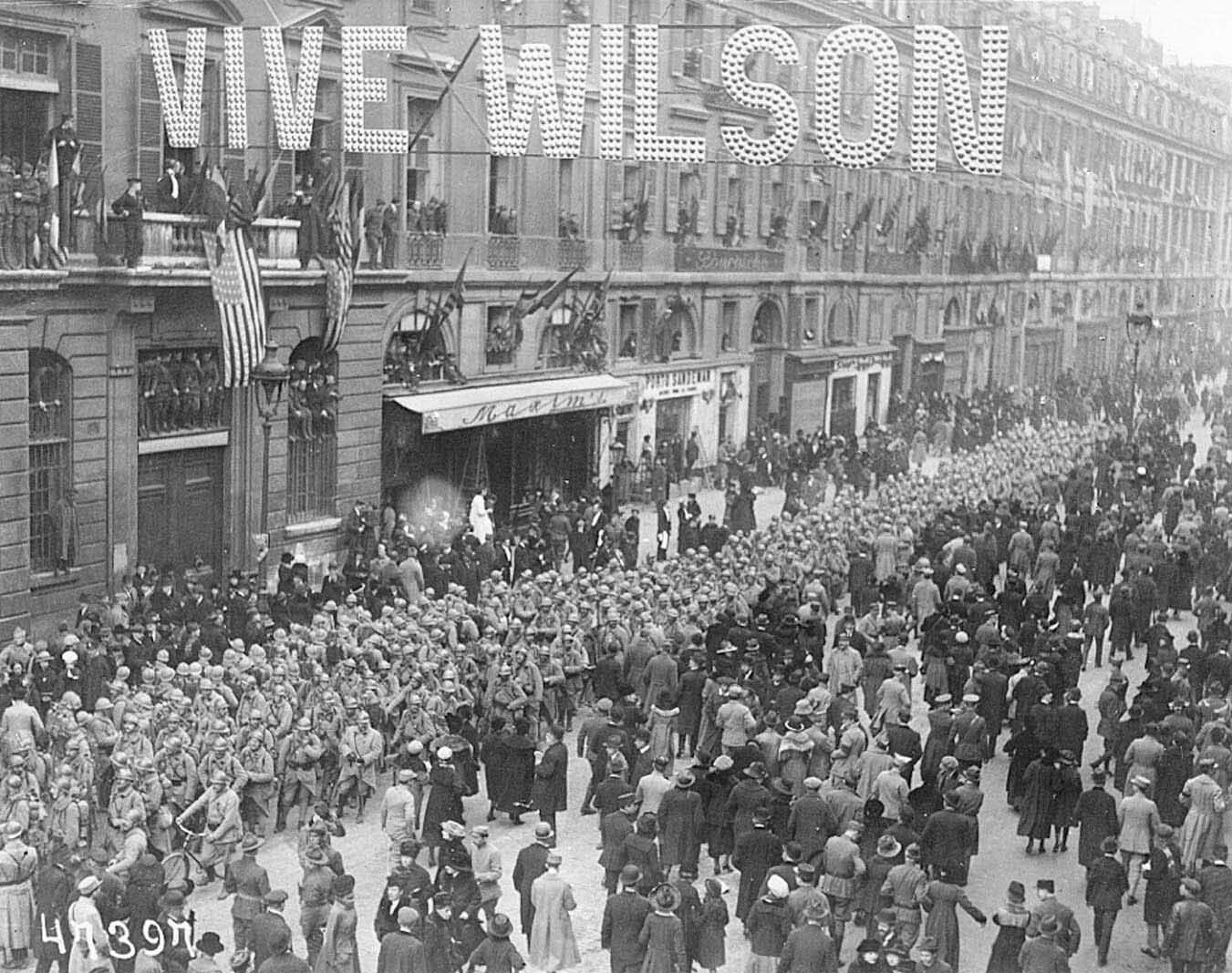 Large crowd marching through a city street beneath a “Vive Wilson” banner, celebrating or supporting a political figure.