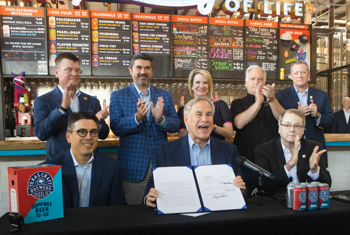 Greg Abbott signs a bill at a craft brewery in Texas, surrounded by state officials and business leaders.