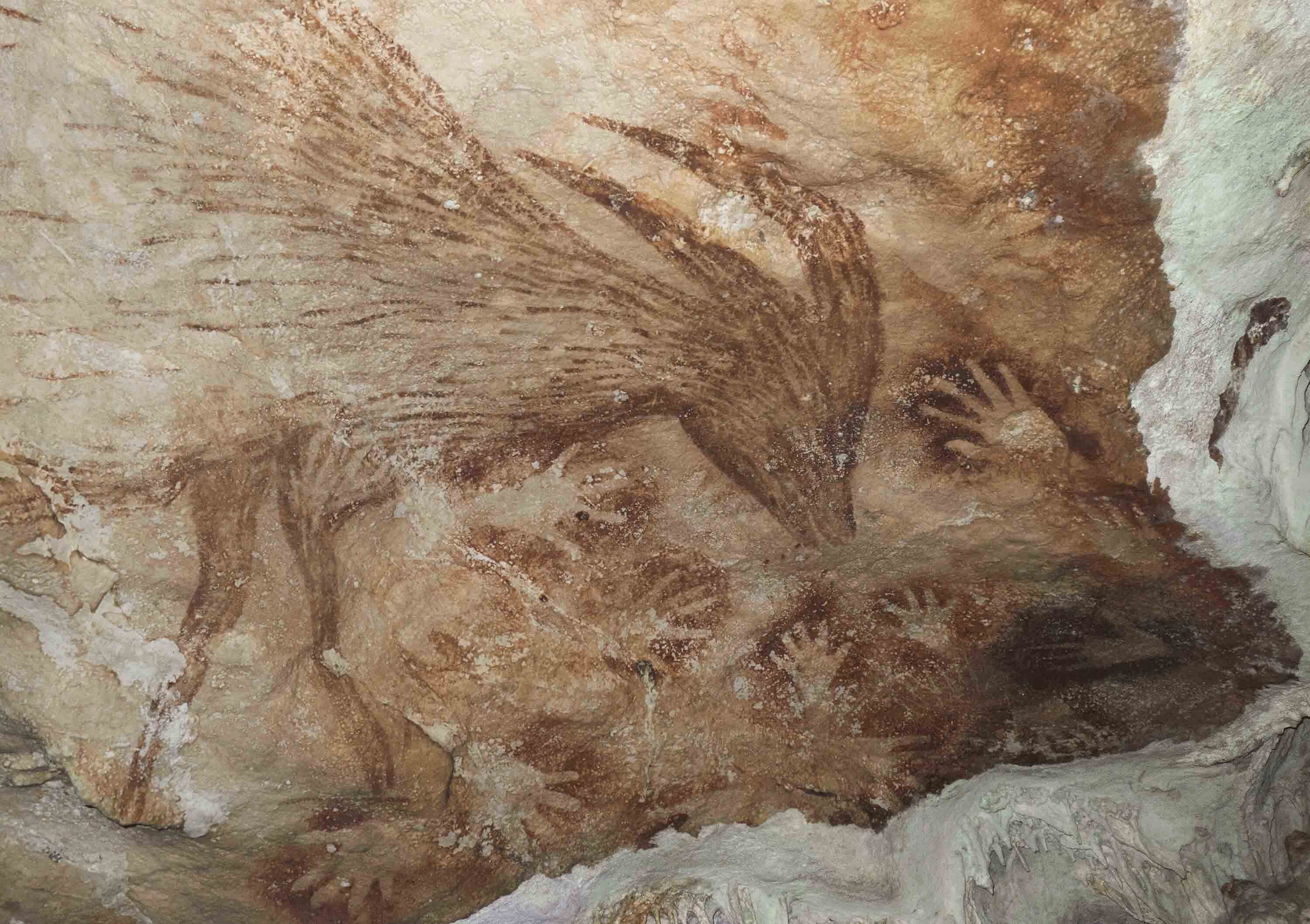 Animal painting and hand stencils on pale cave surface.