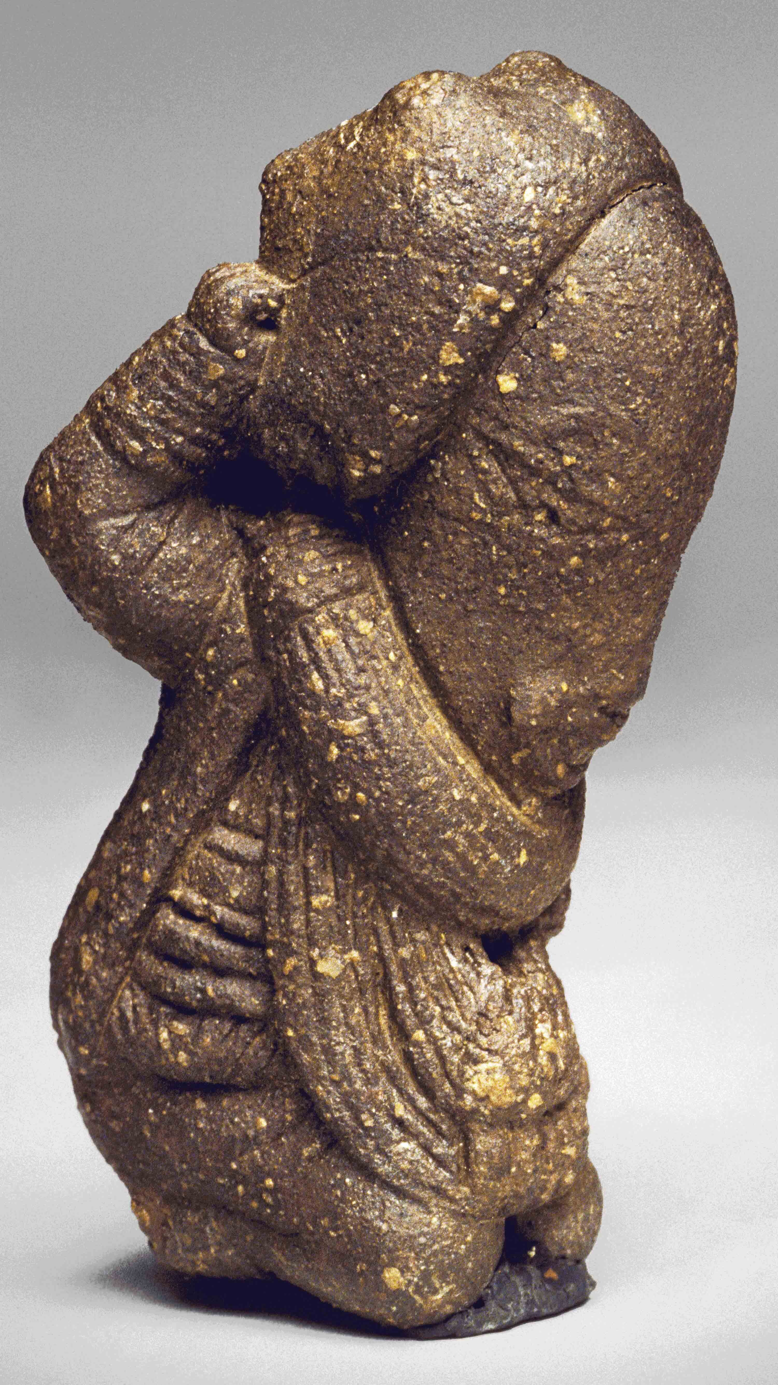 Kneeling figure made of rough textured brown clay.