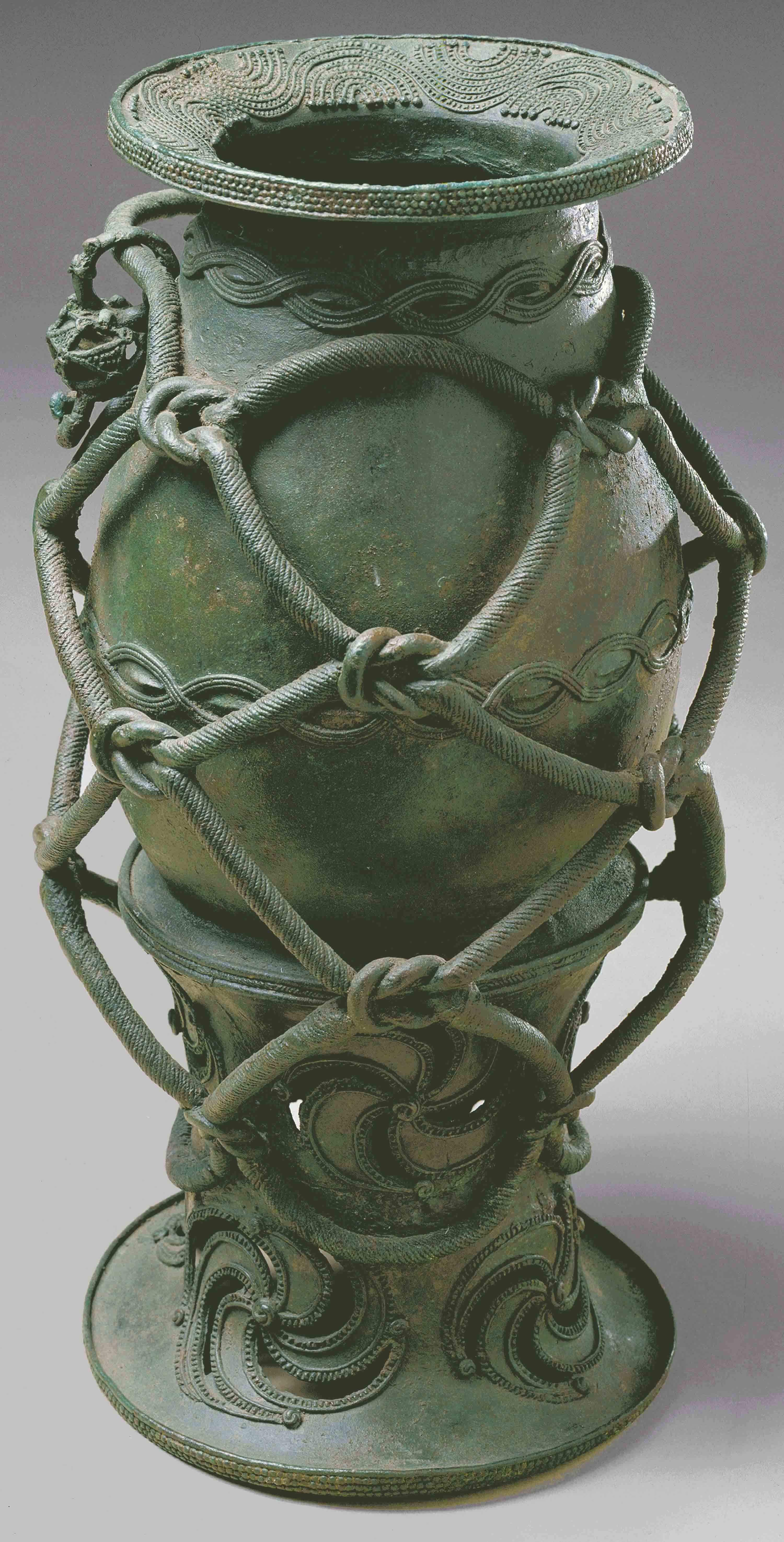 Elaborate pot-like sculpture with gray-green patina.