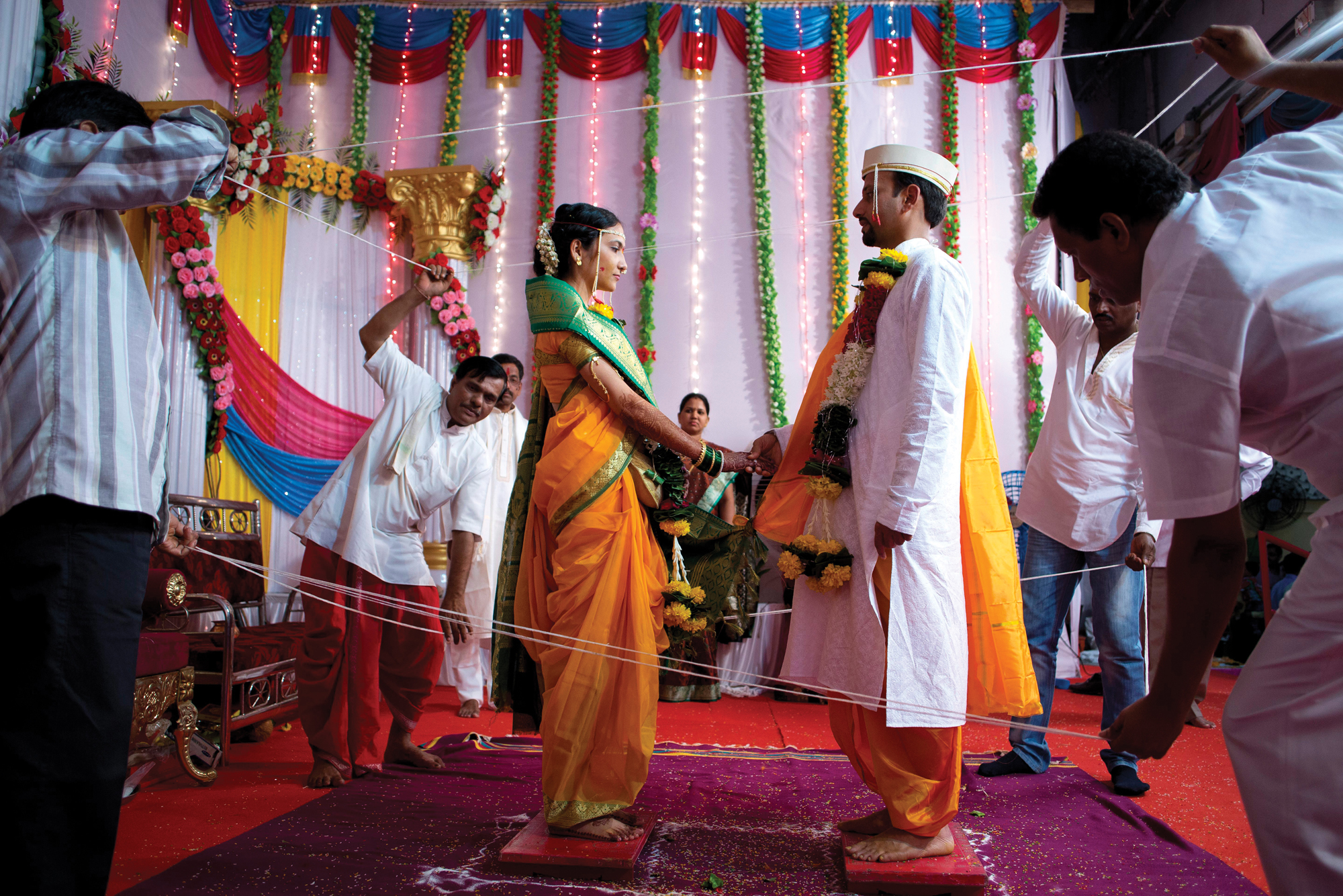 A man and a woman stand on red blocks and face each other, wearing traditional non-Western garb.