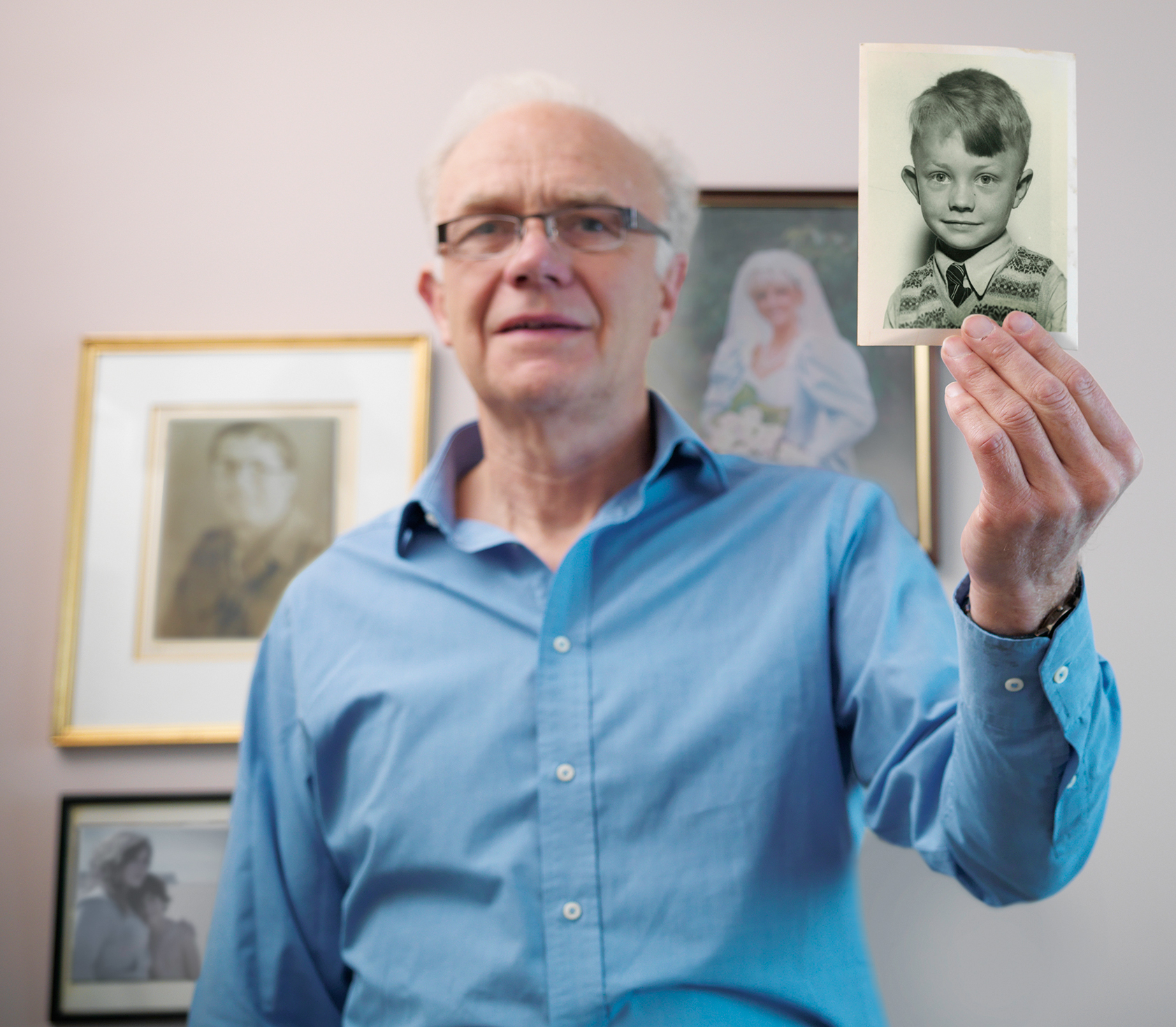 An older man holds up a vintage photograph of a young boy.