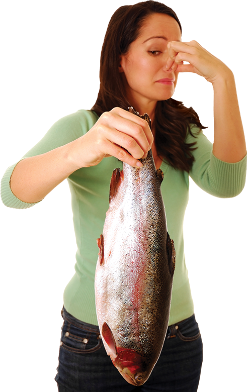 A girl holding a rotten fish in one hand while closing her nose to stop the odor with another hand.