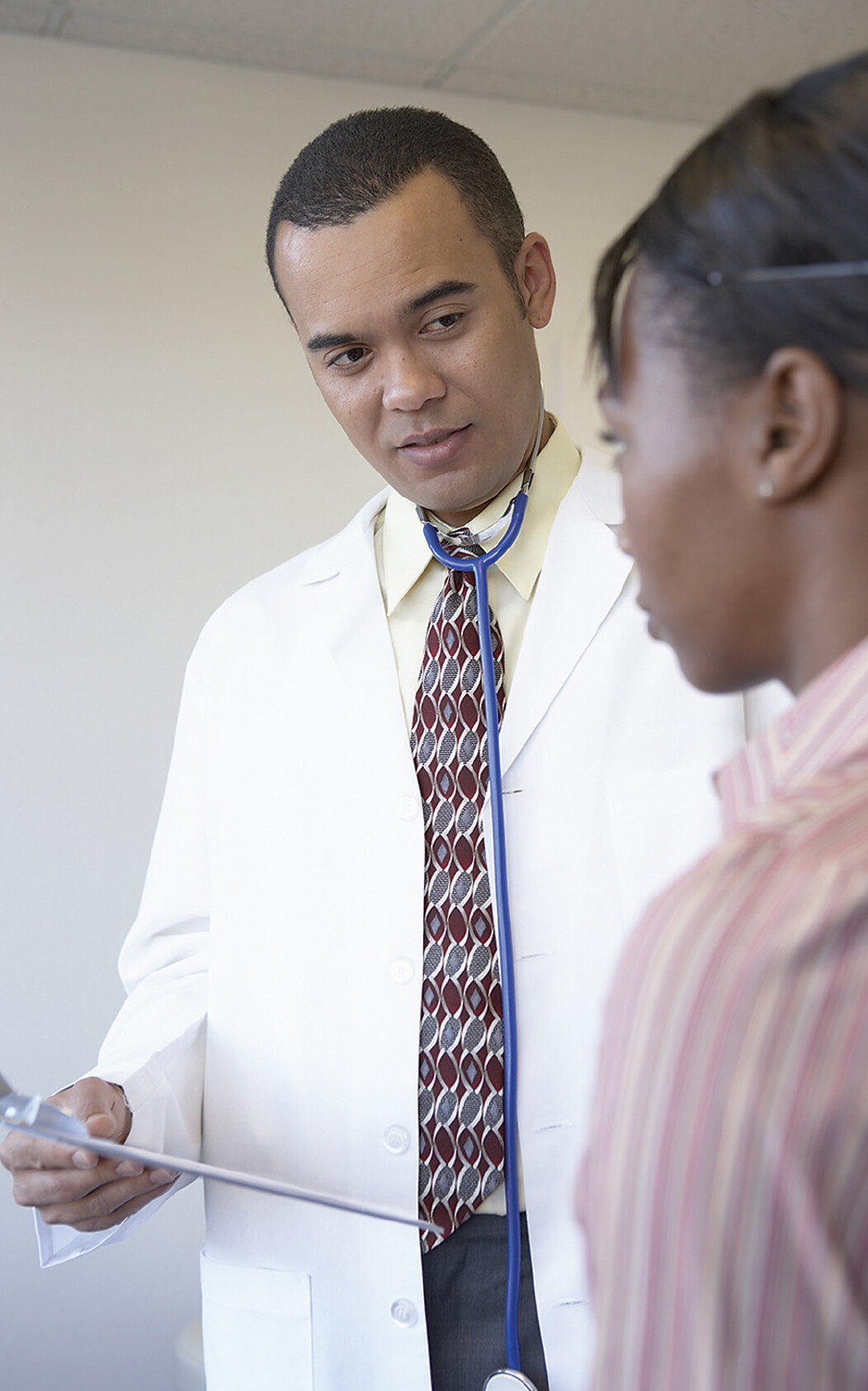 A photo of a doctor holding a clipboard and speaking to a patient.