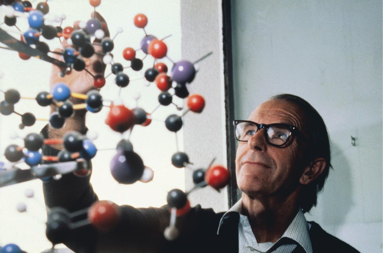 A photo shows Fred Sanger analyzing the structure of a complex ball-and-stick model.