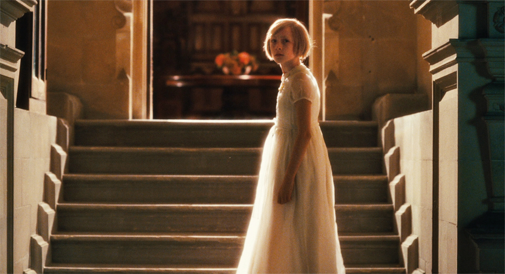 A girl in a dress stands on a stairway in Atonement.