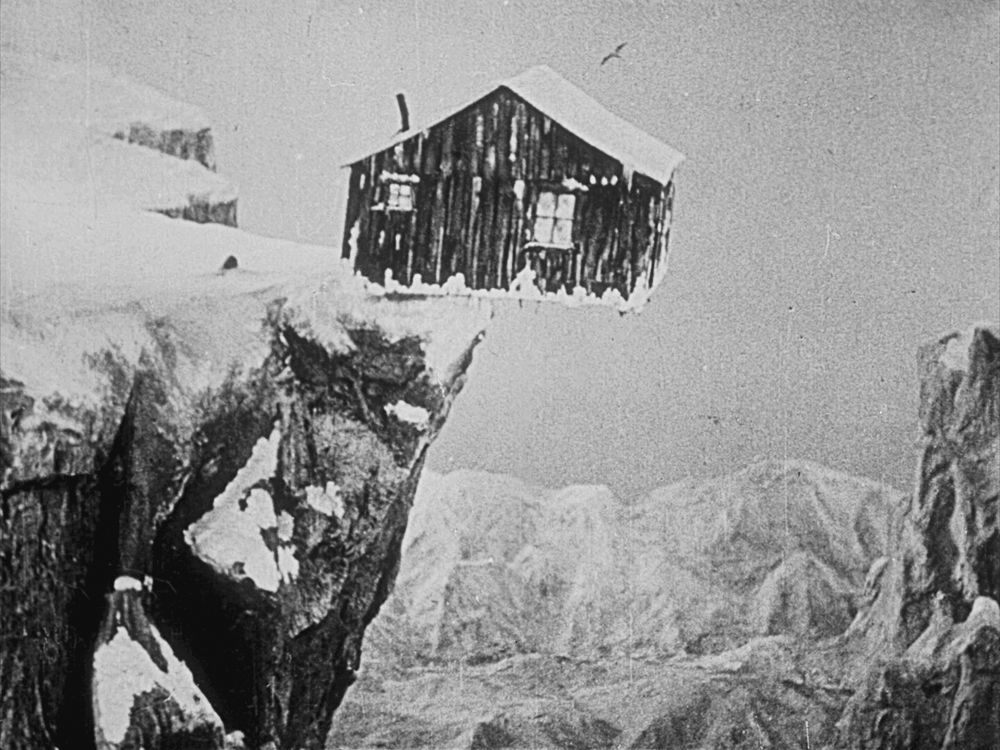 A small wooden house sits precariously on the edge of a snowy cliff in The Gold Rush.