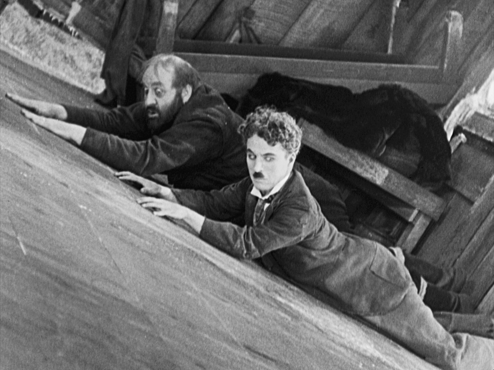 Two men cling to a wooden floor that is tilted sideways in The Gold Rush.