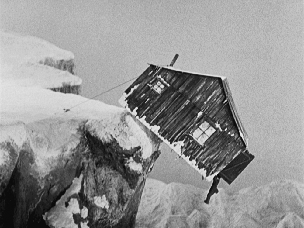 A man hangs out of a door of a cabin that hangs precariously over a snowy cliff in The Gold Rush.