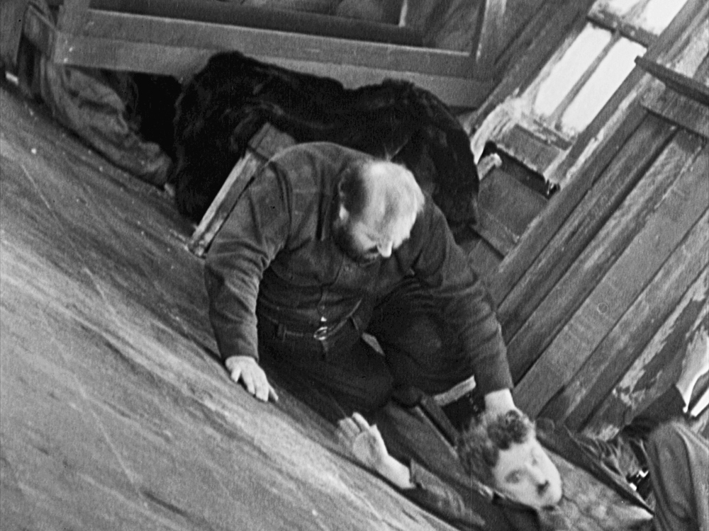 A man helps another man back into the tilted cabin in The Gold Rush.