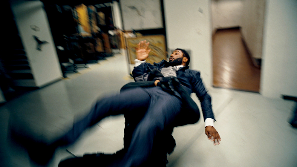 A man in a suit is caught off guard while being attacked by another character in Tenet.