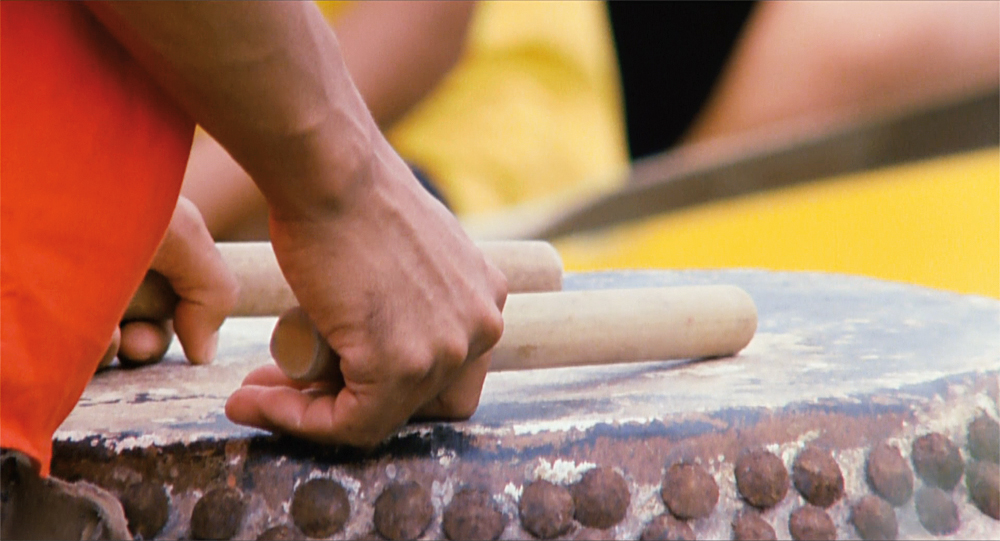 Two hands hold drum sticks over the head of a drum in The Killer.