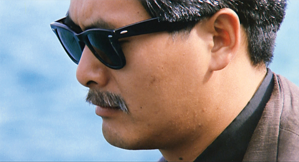 The profile of a man with sunglasses and a moustache looking pensive in The Killer.