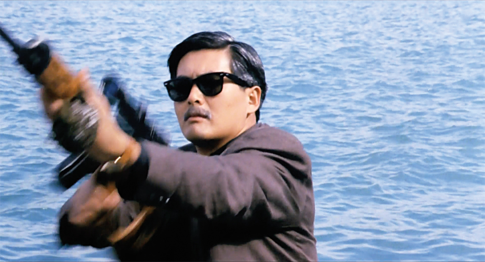 A man with sunglasses and a moustache aims his weapon without using the scope in The Killer.