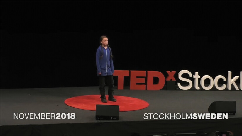A screenshot of Greta Thunberg’s Ted X talk. She stands on a stage in an auditorium.