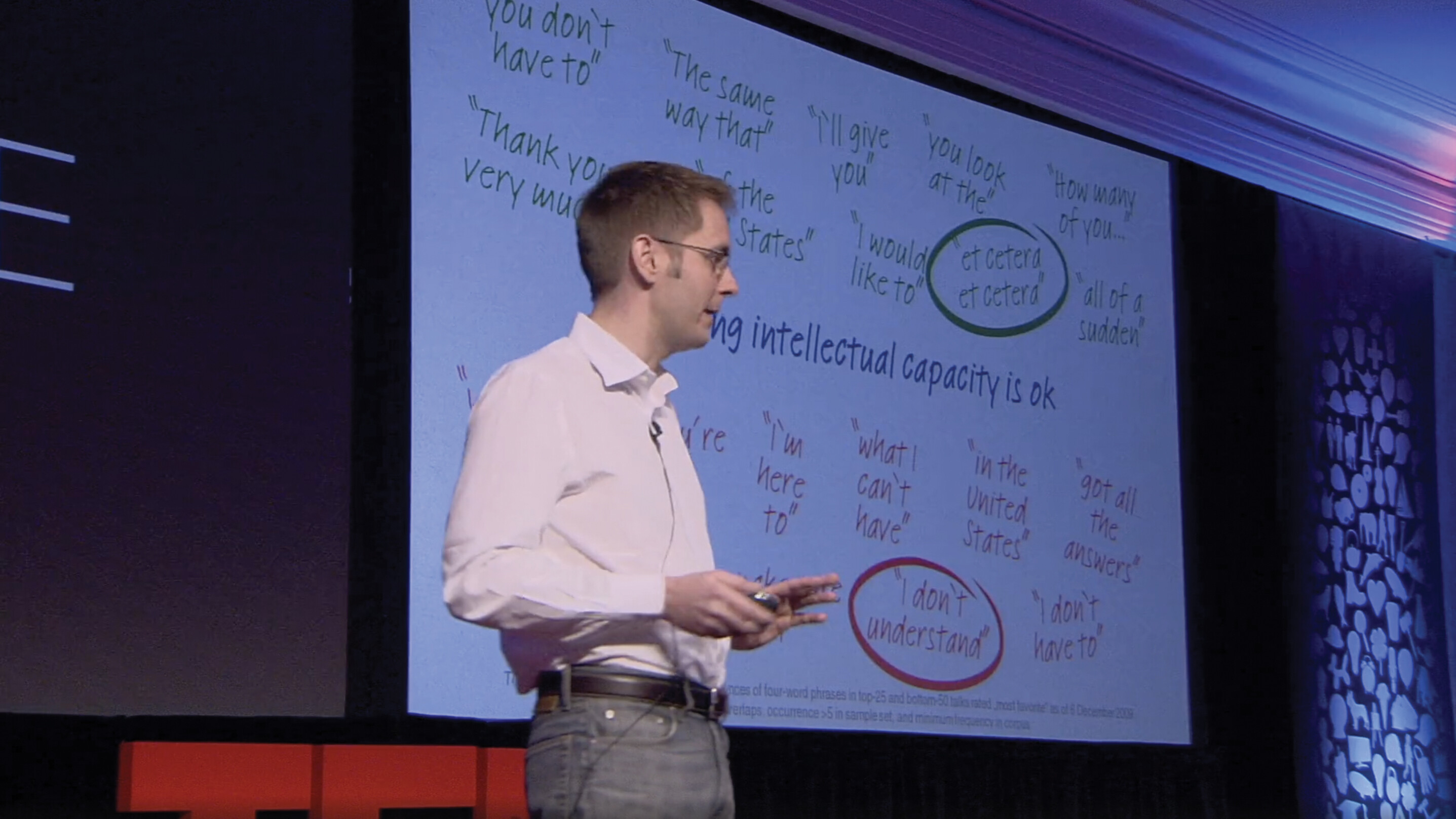 A screenshot of Sebastian Wernicke’s TED talk. He stands on a stage in an auditorium in front of a slide show presentation.