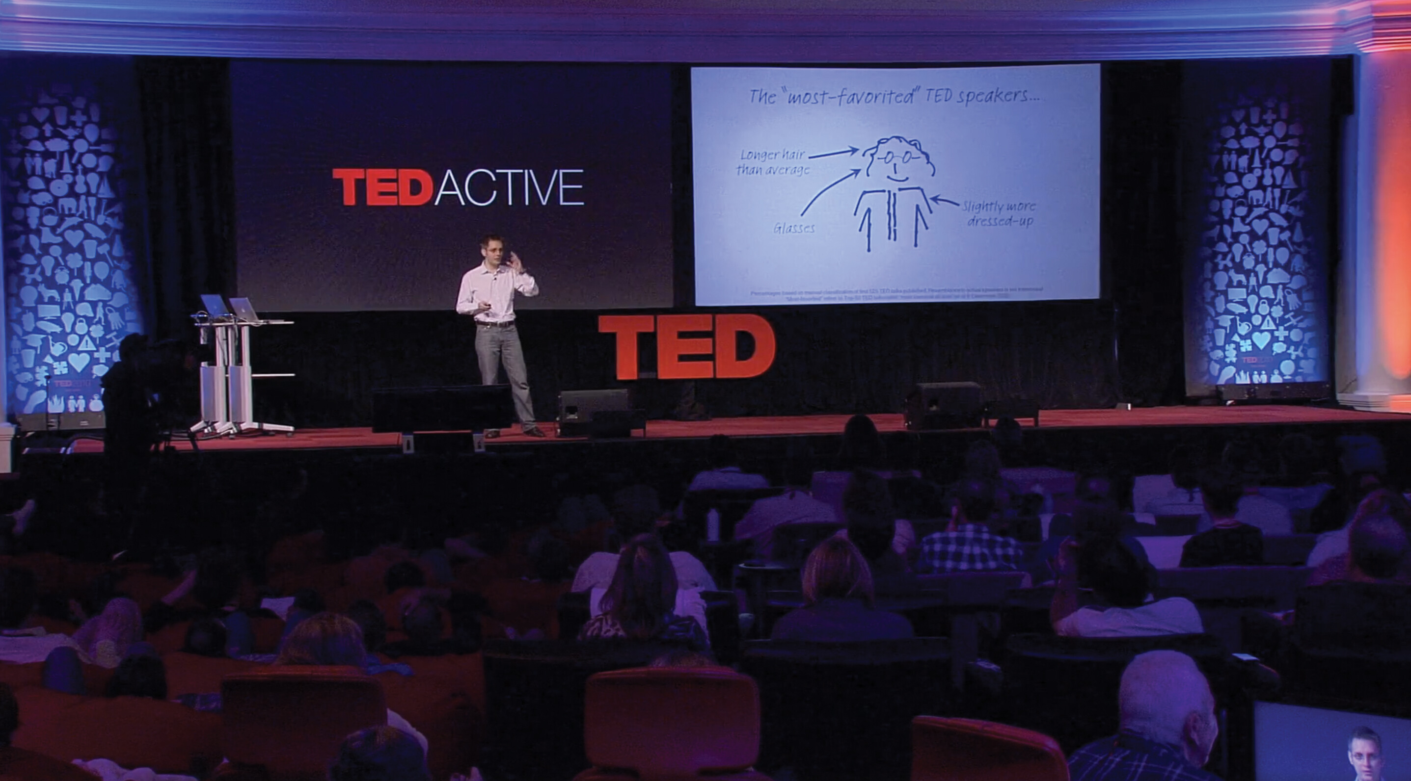 A screenshot of Sebastian Wernicke’s Ted X talk. He stands on a stage in an auditorium in front of a large crowd.