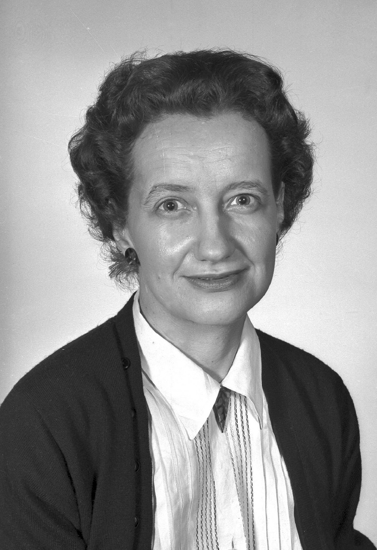 A woman wearing a collared shirt with a jacket over it poses for a picture.